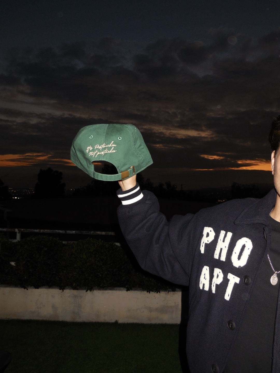 DJ Pistacchio embroidered cap held up against a sunset sky